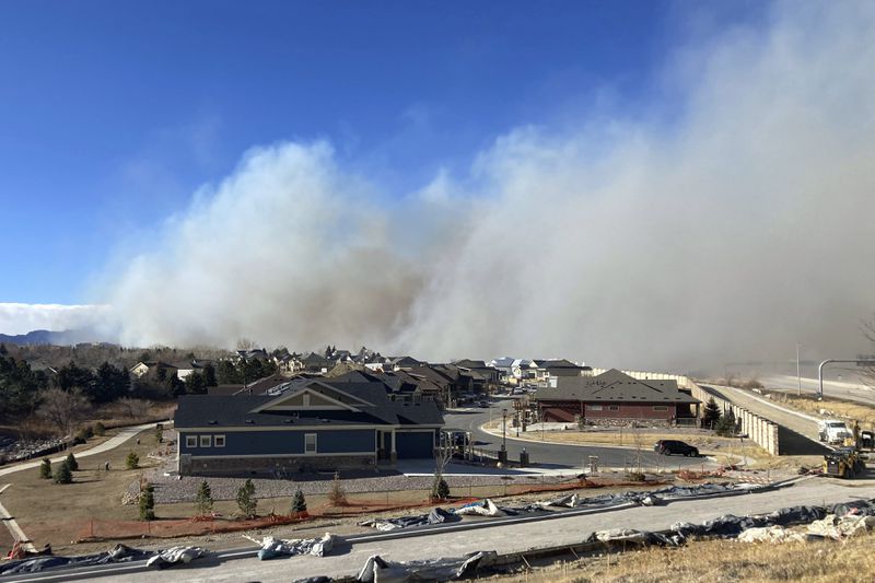 Smoke from a wildfire rises in the background, Thursday, Dec. 30, 2021, in Superior, Colo. All 13,000 residents of the northern Colorado town were ordered to evacuate Thursday because of a wildfire driven by strong winds. (AP Photo/David Zelio)