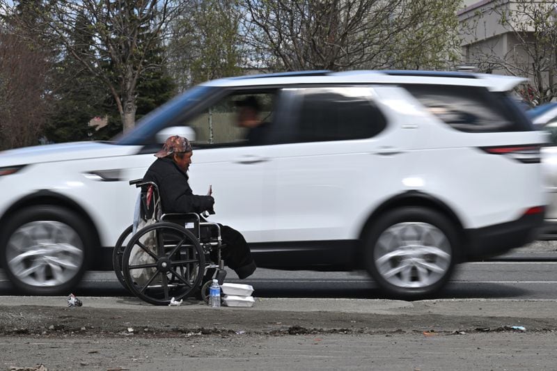 Westbound traffic on Northern Lights flows past a person in a wheelchair holding a sign while panhandling near A Street on Tuesday, May 7, 2024. (Bill Roth / ADN)