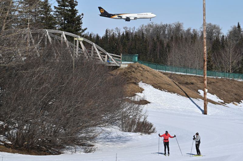Skiers stand on groomed snow in the stadium at Kincaid Park as an UPS Boeing 747-8 freighter en route from Hong Kong lands at Ted Stevens Anchorage International Airport on Sunday, April 14, 2024.  (Bill Roth / ADN)