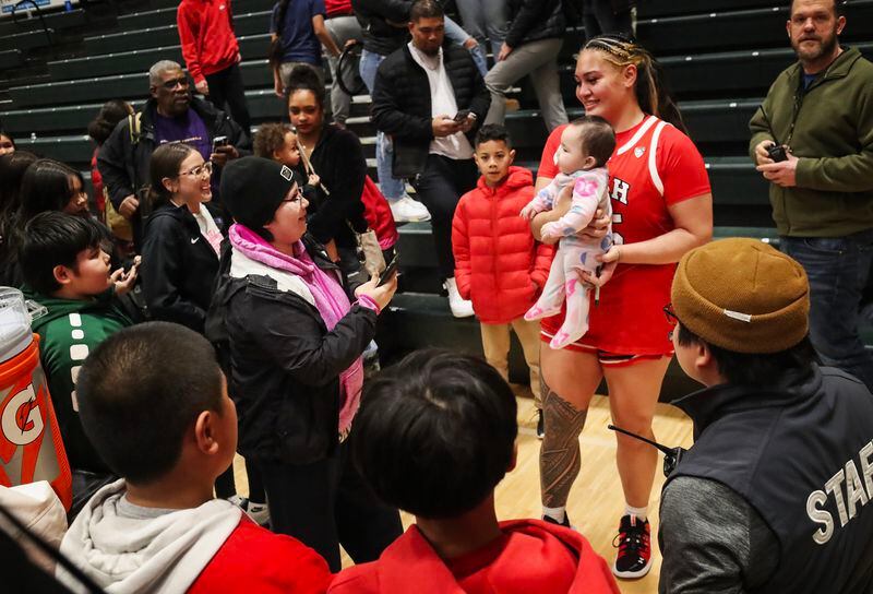 A woman hands her baby to Alissa Pili, a Dimond High School graduate currently playing basketball for the University of Utah, and takes a photo of them together after her game against UAA at the Alaska Airlines Center in Anchorage on Saturday, Nov. 18, 2023. (Emily Mesner / ADN)