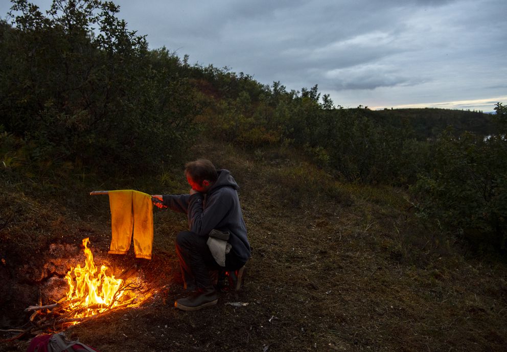 Peter Anthony dries clothes by the fire after a full day in the field. (Washington Post photo by Jonathan Newton)