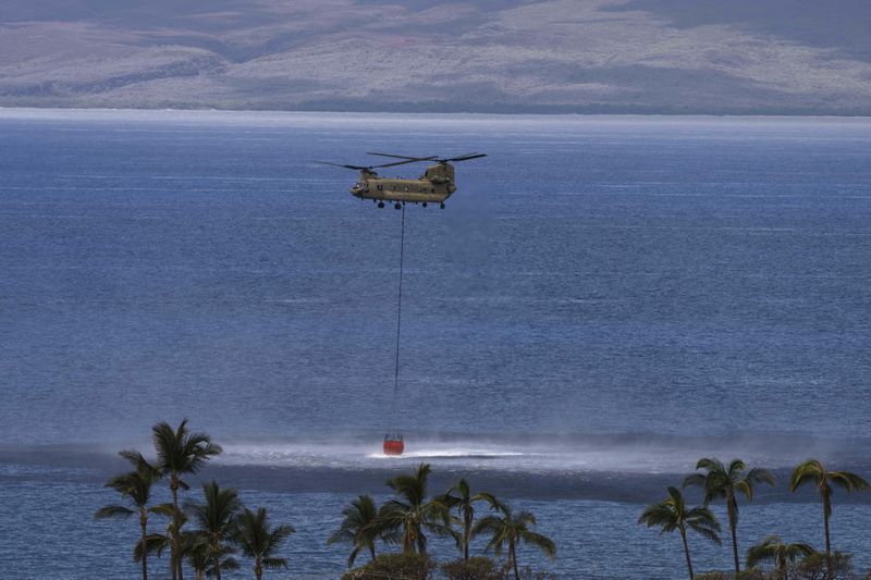 A Chinook helicopter scoops up water from the ocean near Lahaina, Hawaii, Wednesday, Aug. 16, 2023.  (AP Photo/Jae C. Hong, File)