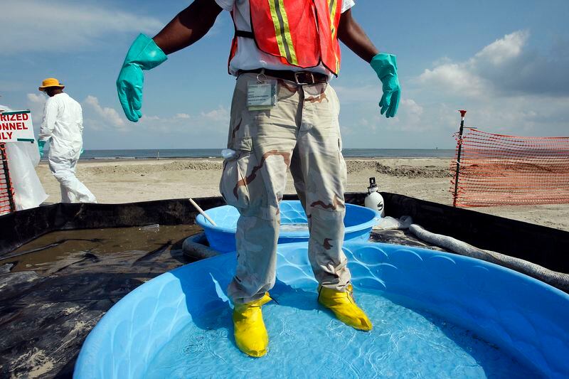 FILE - A worker assisting in the cleanup of oil from the Deepwater Horizon oil spill lets water and detergent drip from his gloves while standing in a decontamination pool on a beach in Grand Isle, La., Aug. 5, 2010. When a deadly explosion destroyed BP's Deepwater Horizon drilling rig in the Gulf of Mexico, tens of thousands of ordinary people were hired to help clean up the environmental devastation. These workers were exposed to crude oil and the chemical dispersant Corexit while picking up tar balls along the shoreline, laying booms from fishing boats to soak up slicks and rescuing oil-covered birds. (AP Photo/Patrick Semansky, File)