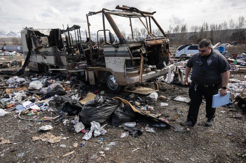 Brian Pavadore of the Anchorage Police Department walks through the homeless encampment and photographs vehicles, including a burned RV. (Marc Lester / ADN)