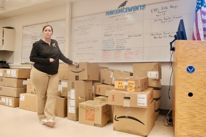 Sgt. Kathryn Manning stands by boxes full of JROTC gear slated to be donated at the end of the year on April 22, 2024. The whiteboard behind her lists her students’ academic and military achievements. (Photo by Claire Stremple/Alaska Beacon)