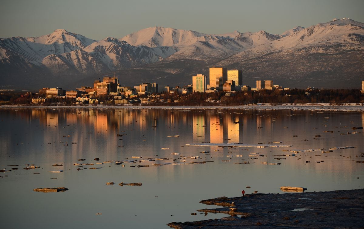 A man and his dog walk on the edge of the ice along Knik Arm with downtown Anchorage and the Chugach Mountains in the background on Tuesday, April 11, 2017. (Bob Hallinen / Alaska Dispatch News)