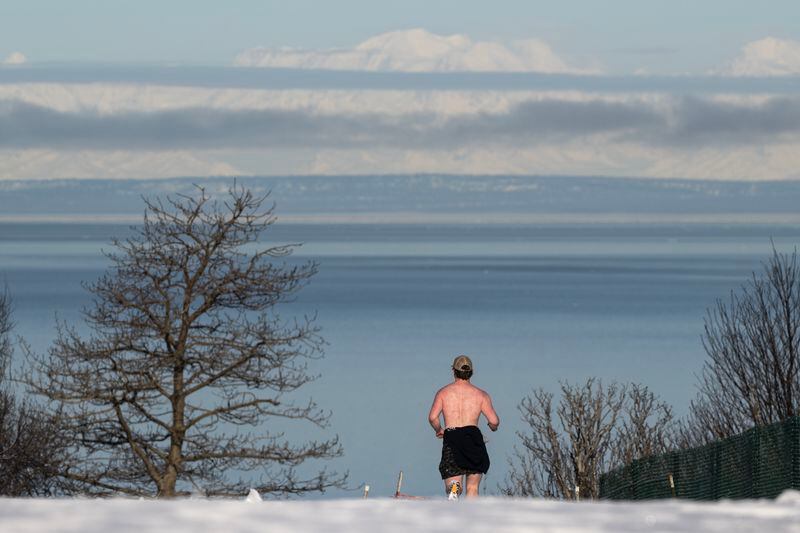 A bit of new overnight snow doesn’t prevent a runner from soaking in the sunshine along the Tony Knowles Coastal Trail near Point Woronzof on April 9, 2024. (Marc Lester / ADN)
