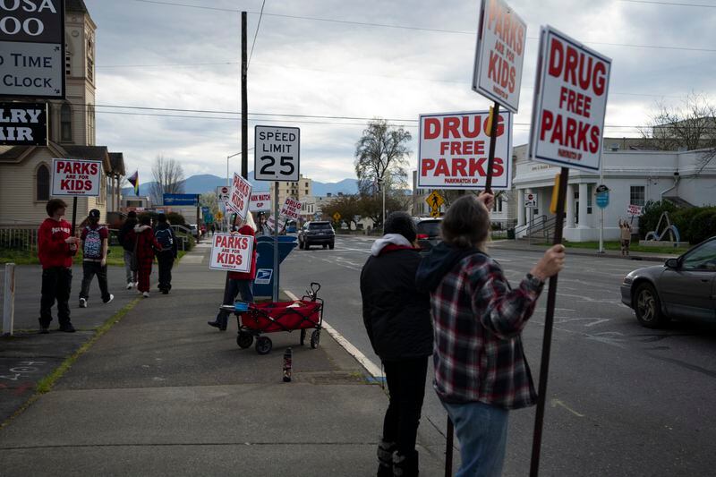 A teenager who was walking by stops to hold a sign as a member of the self-proclaimed "park watch" group walks to speak with them outside City Hall on Wednesday, March 20, 2024, in Grants Pass, Ore. The rural city of Grants Pass in southern Oregon has become the unlikely face of the nation’s homelessness crisis as its case over anti-camping laws goes to the U.S. Supreme Court. The case has broad implications for cities, including whether they can fine or jail people for camping in public. (AP Photo/Jenny Kane)