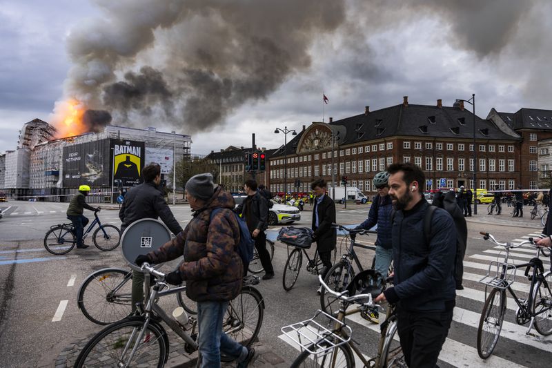 People ride bicycles as smoke rises from the Old Stock Exchange in Copenhagen, Denmark, Tuesday, April 16, 2024. A fire raged through one of Copenhagen’s oldest buildings on Tuesday, causing the collapse of the iconic spire of the 17th-century Old Stock Exchange as passersby rushed to help emergency services save priceless paintings and other valuables. (Emil Nicolai Helms/Ritzau Scanpix via AP)