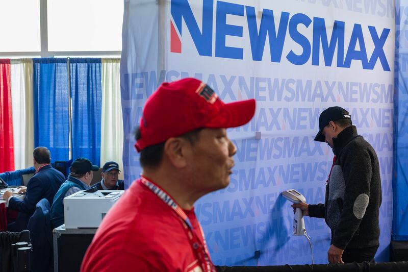 A Newsmax television crew member steam irons a backdrop for the organization during a conservative political conference in National Harbor, Md., on Feb. 24. (Tom Brenner for The Washington Post)
