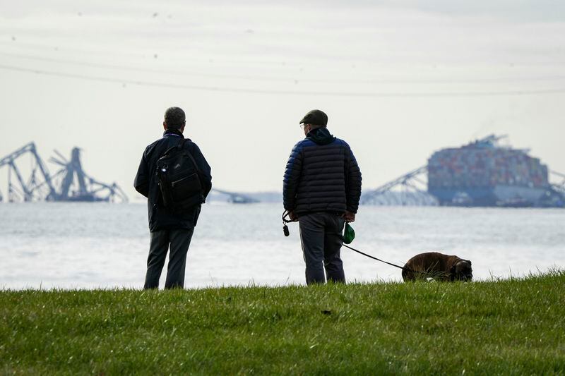 Two men observe the collapsed Francis Scott Key Bridge wreckage from Ft. McHenry, Md., on Tuesday, March 26, 2024. The bridge collapsed early Tuesday morning when a cargo ship collided with it. (Ulysses Muñoz/The Baltimore Banner via AP)