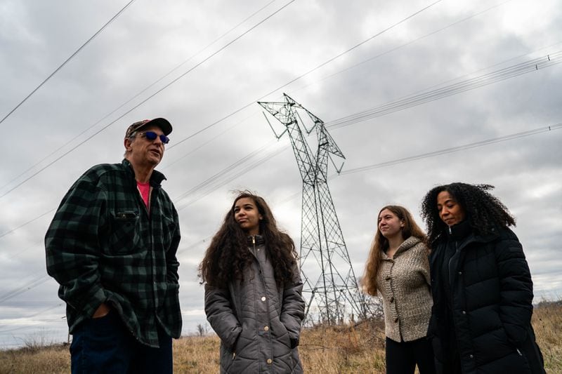 Richard Gee and his wife, Mary, walk along their property with daughters Isabella, 14, and Maria, 16, with transmission lines that abut their land shown behind them in Charles Town, W.Va., in January. (Salwan Georges/The Washington Post)