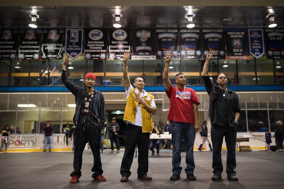 The Fairbanks Four, from left, George Frese, Marvin Roberts, Eugene Vent and Kevin Pease, raise four fingers as a symbol of their struggle during a potlatch held in their honor at the Big Dipper arena in Fairbanks on Oct. 19, 2016. (Loren Holmes / ADN file)