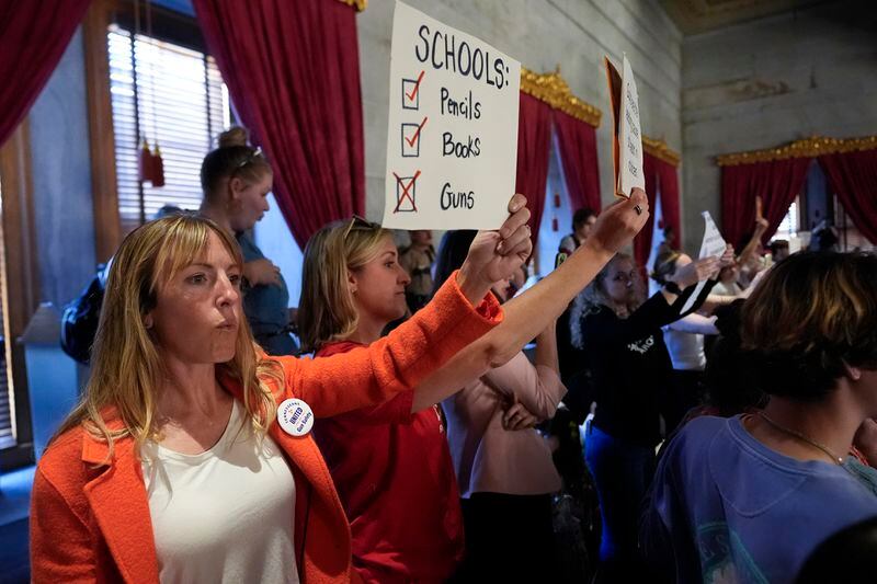Kate Domingues holds a sign in the gallery against a bill that would allow some teachers to be armed in schools during a legislative session in the House chamber Tuesday, April 23, 2024, in Nashville, Tenn. (AP Photo/George Walker IV)