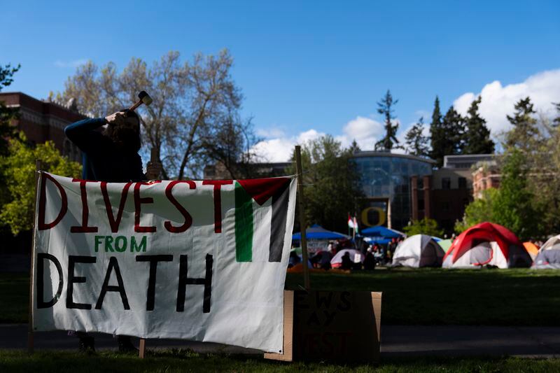 A student at the University of Oregon sets up a sign that reads "Divest from death" as students set up a tent encampment at the university to protest the Israel-Hamas war on Monday, April 29, 2024, in Eugene, Ore. (AP Photo/Jenny Kane)