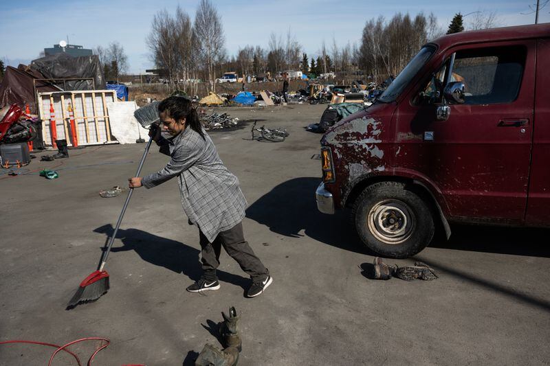 Kaitlin Imboden sweeps as she prepares to leave an extensive encampment near Cuddy Park in Midtown Anchorage on Tuesday before abatement begins. (Marc Lester / ADN)