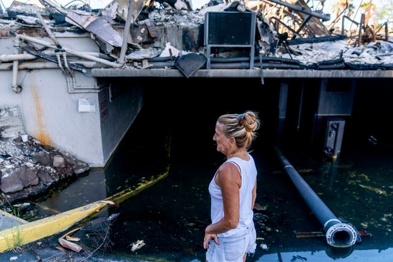 Janet Spreiter, whose home across the street was destroyed in the August wildfire, stands in front of a flooded parking garage in a destroyed business complex next to the Lahaina Shores Beach Resort on Front Street, Friday, Dec. 8, 2023, in Lahaina, Hawaii. (AP Photo/Lindsey Wasson, File)